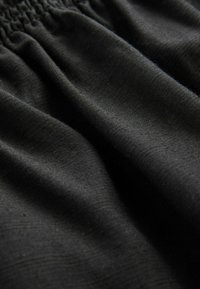 Tissu noir avec une texture lisse, froncé en haut, présentant de subtils motifs délicats. Le matériau semble léger et respirant.
