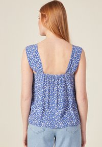 Top sin mangas de flores azules con espalda cuadrada, diseño fruncido y tela texturizada que presenta pequeñas flores blancas y crema.