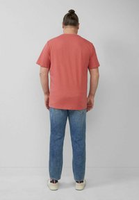 Kurzärmliges, korallenfarbiges T-Shirt mit Rundhalsausschnitt, kombiniert mit hellblauen Jeans. Der Stoff wirkt weich mit einer lässigen Passform, von hinten getragen.