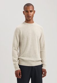 Lichtbeige gebreide trui met een ronde hals, geribde manchetten en zoom. Zachte textuur, reguliere pasvorm en raglanmouwen.