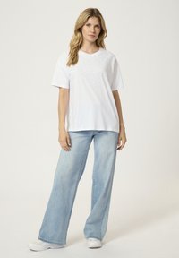 T-shirt blanc à manches courtes avec des strass dispersés sur le devant, associé à un jean large bleu clair et des baskets blanches.