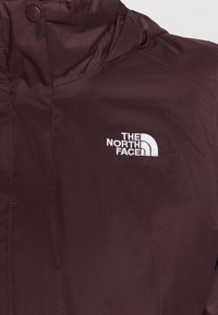 Bordeauxrode jas met een gladde textuur, voorzien van een hoge kraag en rits. Het North Face-logo is in het wit op de borst geborduurd.