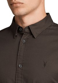 Camisa marrón de algodón mezclado con botones, con cuello estructurado, dos botones en el cuello y un bordado sutil del logo en el pecho.