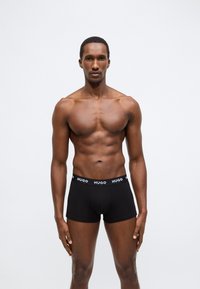 Slip uomo nero Hugo con cintura elastica con logo, design aderente, realizzato in tessuto liscio, indossato da un modello maschile con fisico tonico.