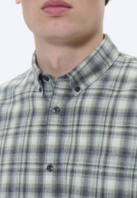Zeleno-sivý kockovaný košeľový top s golierom, so svetlými gombíkmi a mäkkou, textúrovanou tkaninou. Detailný pohľad na výstrih.