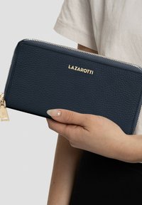 Cartera de cuero azul marino con superficie texturizada, logo dorado "LAZAROTTI" y cierre con cremallera que incluye un charm decorativo.