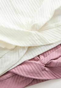 Drei gefaltete Textilien: ein weißer gerippter Stoff oben, ein sanfter rosa gerippter Stoff darunter und ein helles mauve gerippter Stoff darunter, alle mit einer glatten Textur.