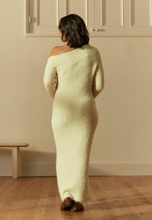 Robe en tricot longue de couleur crème avec une finition texturée, au design décolleté, et aux manches décontractées ; portée avec des chaussures à imprimé léopard.