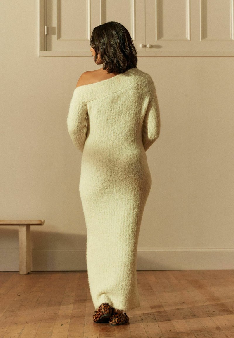 Robe en tricot longue de couleur crème avec une finition texturée, au design décolleté, et aux manches décontractées ; portée avec des chaussures à imprimé léopard.