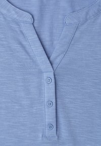 Lyseblå knappeskjorte med tre knapper, blødt tekstureret stof og enkle kravedetaljer.