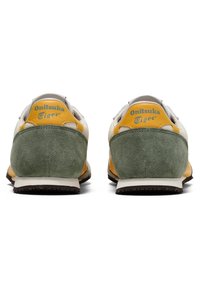 Onitsuka Tiger-sneakers har en blandning av grön mocka och gula läderaccenter på en vit ovandel, med en brun gummisula och logotyp på hälen.