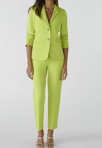 Blazer ajusté vert lime avec deux boutons et poches avant, assorti à un pantalon slim. Tissu lisse, design épuré, style minimaliste.