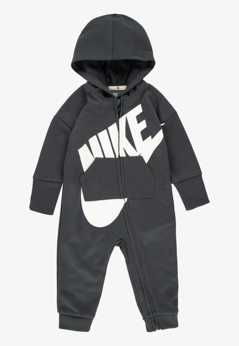 Šedý mikinový overal s veľkým bielym logom Nike, predným zipsom a prednou vreckom. Vyrobený z mäkkej látky s rebrovanými manžetami.