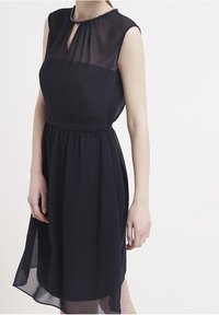 Abito senza maniche blu navy con sovrapposizione trasparente, scollatura a fessura, impreziosito da un bordo di perline, e una cintura arricciata che scende fino a una gonna di lunghezza al ginocchio.