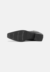 Musta nahkasaapas, jossa on teksturoitu kumipohja ja tukevan korko. Ominaisuuksiin kuuluu sileät pinnat ja virtaviivainen muotoilu.