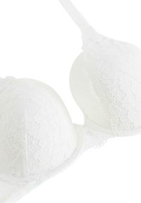Witte kanten beha met gepadde cups, verstelbare banden en een bloemenpatroon. De ingewikkelde kantdetails voegen textuur toe aan de gladde stof.
