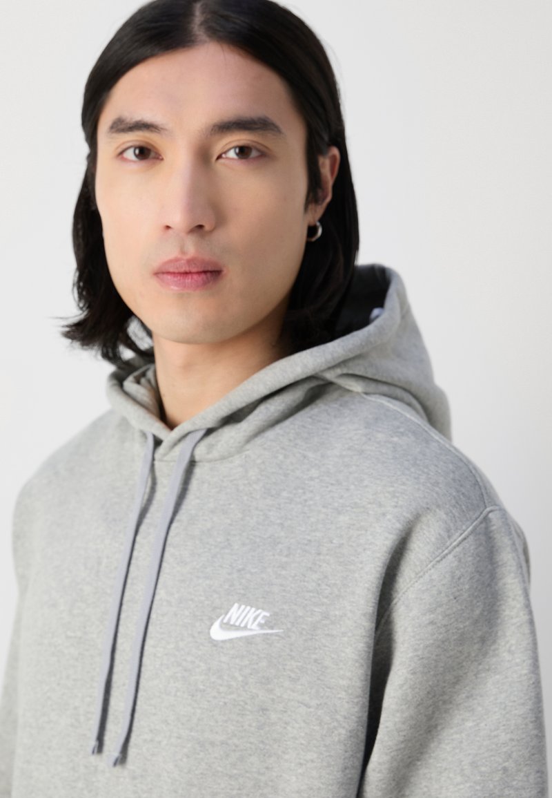 Grauer Hoodie aus weichem Stoff, mit Kapuze und Kordelzug, langen Ärmeln und einem weißen Nike-Logo auf der Brust. Weiche Textur, sportlicher Schnitt.