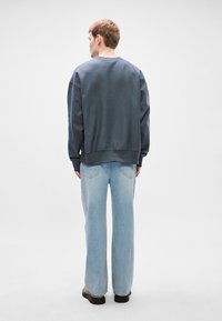 Sweatshirt oversized em algodão azul escuro, combinado com jeans de perna reta azul claro. O design apresenta um decote redondo e punhos canelados.