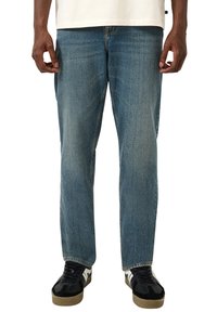 Niebieskie jeansy denimowe o prostym kroju, z jasnym wykończeniem, subtelną fakturą i standardowym fasonem z pięcioma kieszeniami. Noszone z czarnymi trampkami.
