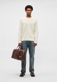 Bēšs džemperis ar garām piedurknēm, gaiši zilas džinsas un tumši brūna ādas soma. Somai ir dubultas rokturi un rāvējslēdzēja aizdare. Melni apavi.