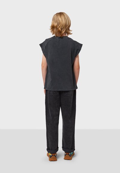 Camiseta de algodón negra con mangas tipo gorra, corte holgado y dobladillo curvado; combinada con pantalones de mezclilla oscuros y zapatillas marrones con acentos coloridos.