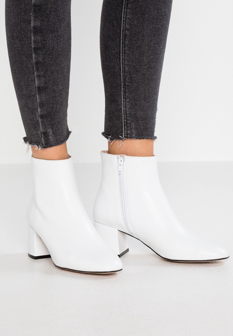 Bottines blanches à finition en cuir lisse, talons carrés et fermeture éclair latérale, assorties à un jean skinny noir à ourlet effiloché.