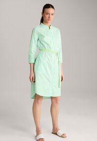 Grünes und weißes gestreiftes Hemdkleid mit langen Ärmeln, Knopfleiste und selbstgebundenem Gürtel. Hergestellt aus leichtem Stoff mit leicht geschwungenem Saum.