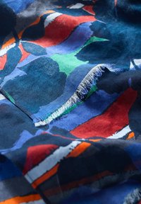 Baumwollstoff mit einem auffälligen, abstrakten Muster in Dunkelblau, Rot, Grün und Weiß sowie ausgefransten Kanten. Glatte Textur.