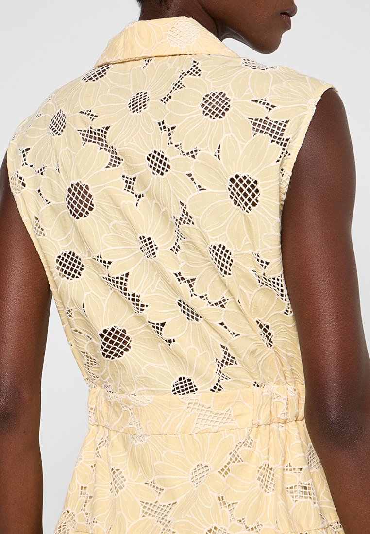 Vestido de encaje amarillo con patrón floral, que presenta un cuello y un diseño sin mangas. La textura parece delicada con acentuaciones de tejido abierto.