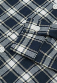 Camisa de cuadros en azul marino de mezcla de algodón; cuenta con cuadros en blanco y beige, cierre de botones, detalle en los puños con botones blancos y una textura suave.