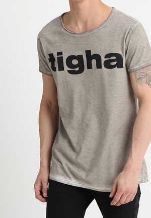 Graues T-Shirt mit kurzen Ärmeln und rundem Halsausschnitt, auf dem in großen schwarzen Buchstaben "tigah." steht. Der Stoff sieht leicht strukturiert und abgenutzt aus.
