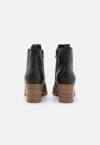 Černé kožené kotníkové boty s texturovaným povrchem, s robustní dřevěnou podrážkou a bočním zipem. Klasický zaoblený tvar, minimalistický design.