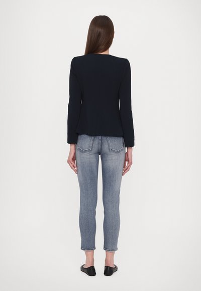 Zwarte op maat gemaakte blazer met lange mouwen, gecombineerd met lichtblauwe skinny jeans, gezien van achteren. Gelaagd stof, slim fit ontwerp.