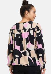 Langärmlige Bluse in Schwarz mit einem abstrakten Muster in Beige, Pink und Weiß. Weicher Stoff mit lockerer Passform und abgerundetem Saum.