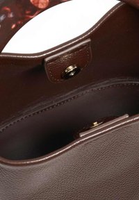 Intérieur d'un sac à main en cuir marron avec une texture lisse, fermeture à pression en matériau doré et doublure douce. Design ouvert en haut sans compartiments supplémentaires.