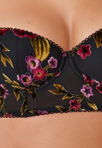 Reggiseno nero senza spalline con un motivo floreale in velluto nelle tonalità di rosa e verde, con bordi ondulati e design delle coppe strutturato.