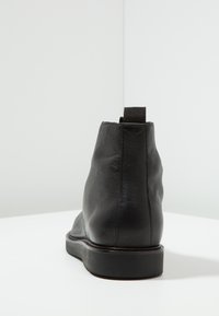 Černá kožená kotníková bota s hladkým povrchem, zaoblenou špičkou, minimalistickým designem a poutkem na zadní straně. Plochá gumová podešev.