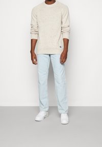 Beige prickig stickad tröja med ribbade ärmslut och nederkant, i kombination med ljusblå raka jeans och vita sneakers.