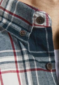 Karokragen eines karierten Hemdes in Dunkelblau, Rot und Weiß mit zwei braunen Knöpfen und einer weichen Stofftextur.