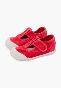 Scarpe da ginnastica rosse in tela con punta rotonda, cinturino in Velcro e suola in gomma bianca con dettagli testurizzati. Progettate con aperture sui lati.