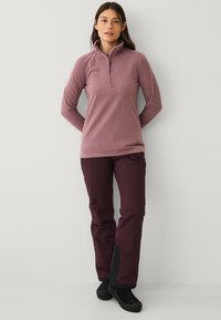 Fleece-pullover i blød mauve med en halvlynlås og krave, parret med mørk maroon vandtætte bukser med sorte ankeldetaljer.