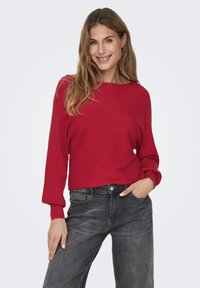 Red ribbed sweater with a wide neckline and long sleeves, paired with gray denim jeans. The textures are soft, creating a relaxed fit.