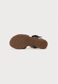 Black sandal with two adjustable straps, rubber sole featuring a wavy pattern, and brown textured outsole. Lightweight design for comfort.