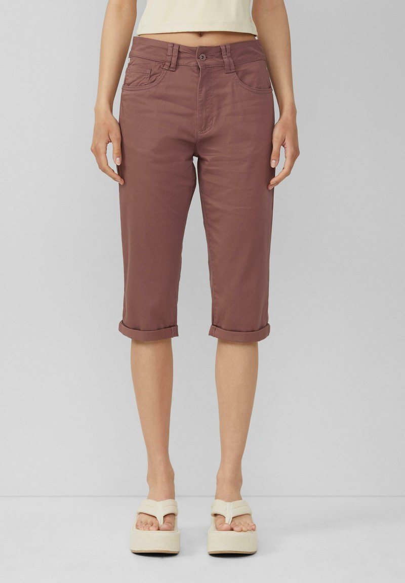 Bordowe spodnie cropped z podwiniętymi mankietami, wykonane z gładkiego materiału, z przednimi kieszeniami i zapięciem na guzik. Połączone z sandałami na platformie.