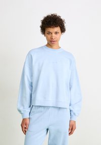 Sweat-shirt bleu clair en coton doux, doté d'un col rond, de manches tombantes et de poignets côtelés. Design minimaliste avec un logo discret.