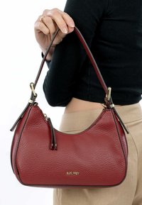 Rodeleren handtas met een gestructureerde afwerking, gebogen silhouet en hardware in goudkleur. Voorzien van een korte strap en een subtiel merkembleem.