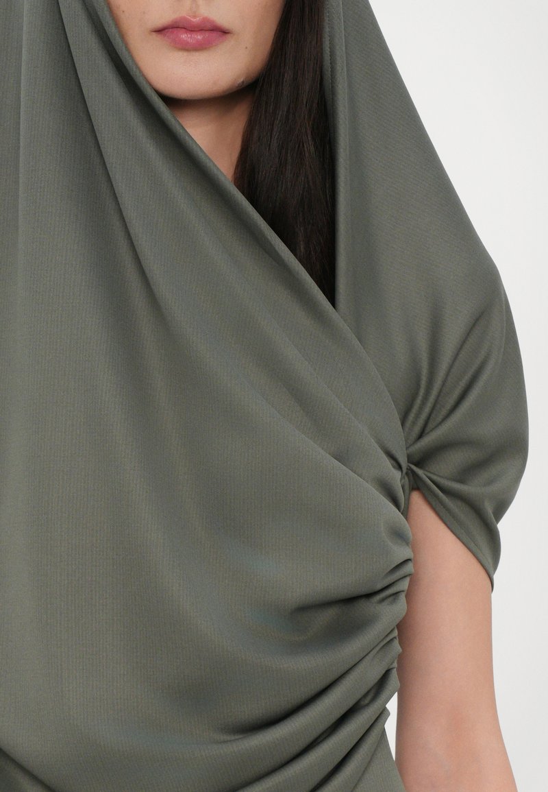 Green draped top made from soft fabric, featuring a twisted design and short sleeves, with subtle vertical ribbed texture.