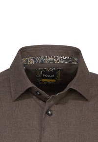 Camicia marrone con bottoni, realizzata in un tessuto testurizzato. Il colletto interno presenta una fodera decorata in oro e nero, con un'etichetta visibile.