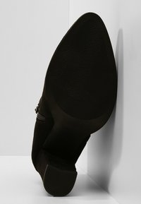 Botín negro de ante hasta el tobillo con suela curvada y texturizada, que cuenta con un zip lateral y un tacón apilado para mayor estabilidad y diseño.