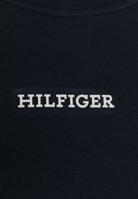 Tessuto di cotone blu navy con il testo "HILFIGER" in lettere bianche in grassetto, posizionato centralmente, con una trama liscia e uniforme.